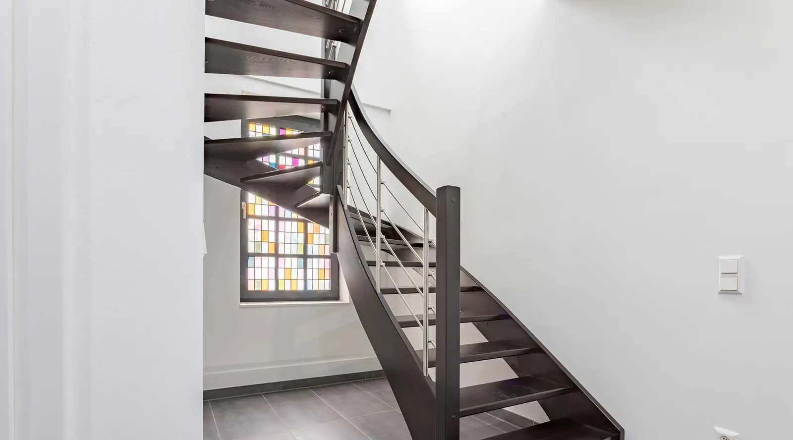 Gewendelte dunkle Treppe mit Buntglasfenster im Gründerhaus